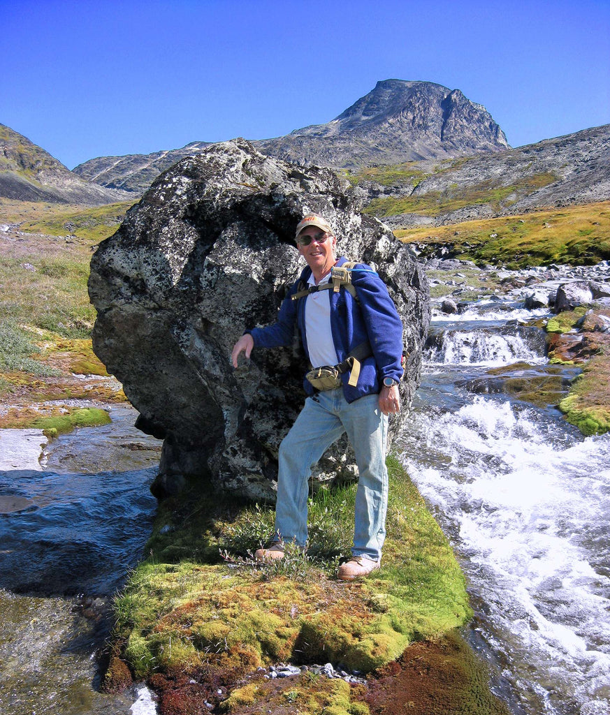 A person standing in front of a boulder next to a stream of water