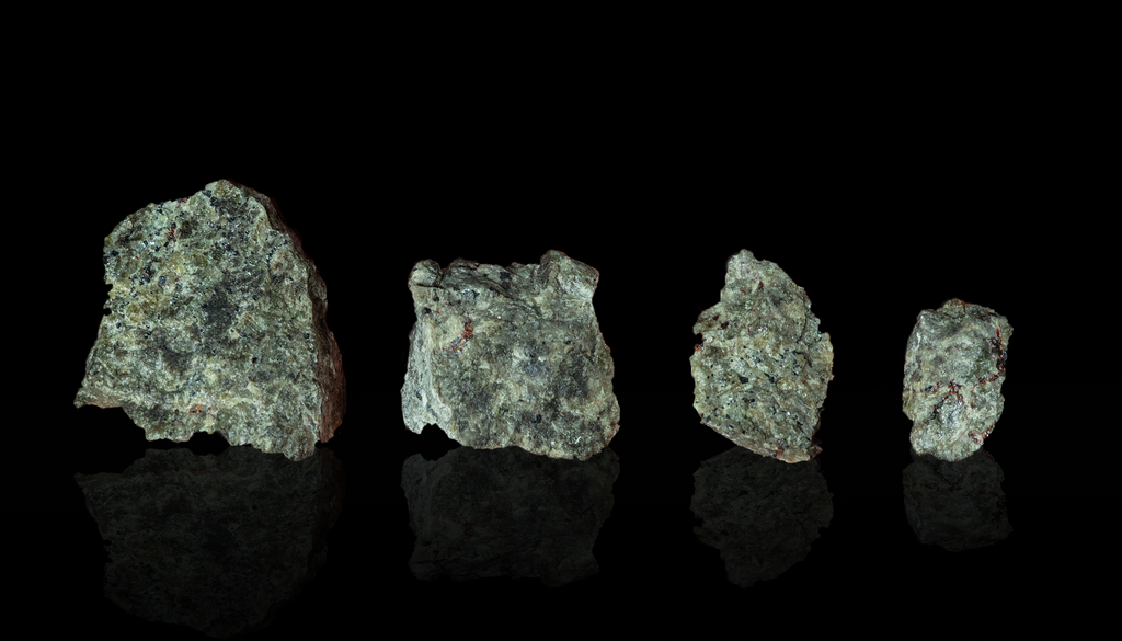 Four dark green rocks on a black reflective surface