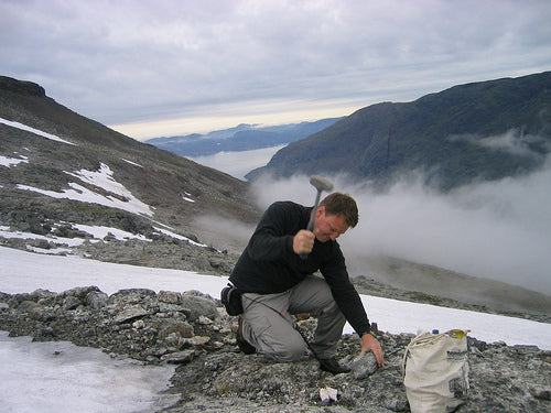 A guy hitting a rock with hammer in the mountains of Greenland