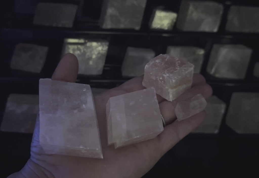 A hand holding four pink translucent calcite crystal against a black background. UV reactive pink.